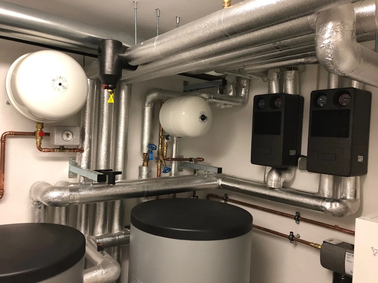 Heizungsraum mit Ausdehnungsgefäßen, gedämmten Leitungen, Pumpengruppen und Speicher